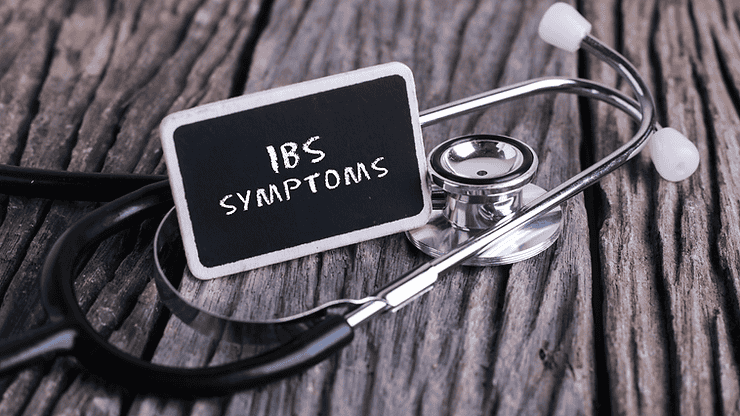 IBS symptoms written on a small chalkboard next to a stethoscope on a wooden surface, emphasizing the focus on Irritable Bowel Syndrome management and gut health.