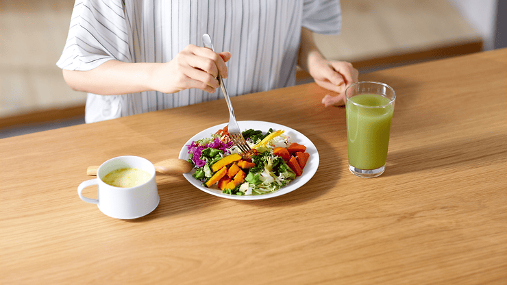 Person eating a colorful salad with mixed vegetables, alongside a green drink and a bowl of soup, emphasizing healthy eating for gut health management related to IBS.