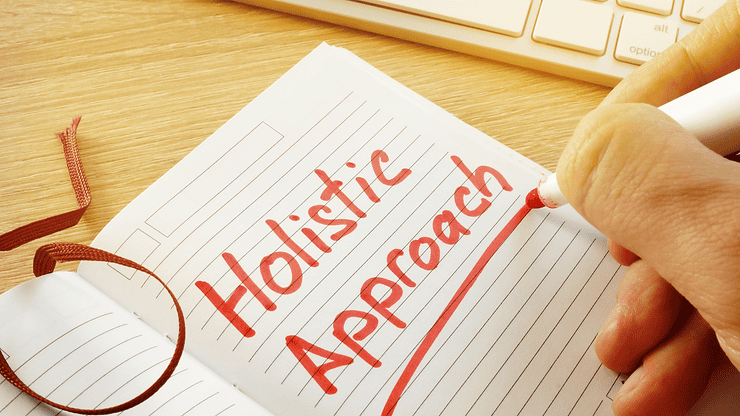 Hand writing "Holistic Approach" in red on an open notebook, symbolizing functional medicine strategies for managing Irritable Bowel Syndrome (IBS) and promoting gut health.