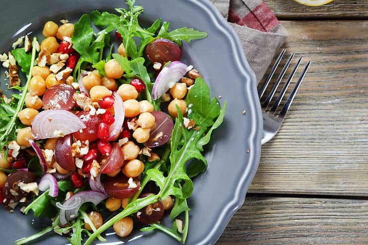 Salad with arugula, chickpeas, grapes, pomegranate seeds, and nuts in a gray bowl, emphasizing healthy eating for managing bloating and digestive health.