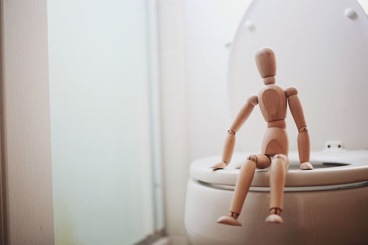 Wooden mannequin sitting on a toilet, symbolizing issues related to constipation and digestive health, relevant to gut health discussions.