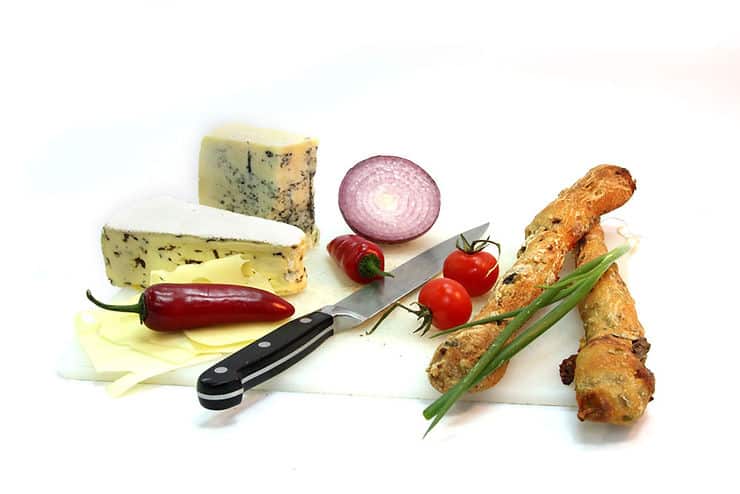 Cheese varieties, fresh vegetables, and herbs arranged on a cutting board with a knife, illustrating ingredients for a low FODMAP diet.