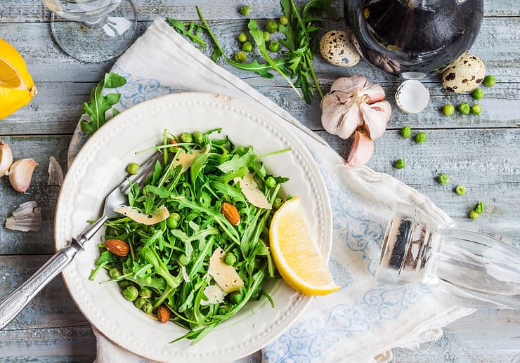 Fresh arugula salad with peas, almonds, and lemon, surrounded by garlic and quail eggs, emphasizing healthy dietary options for managing constipation in IBS.