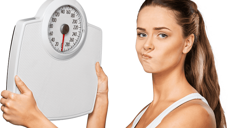 Woman holding a scale with a concerned expression, illustrating the impact of gut health and IBS on weight management.