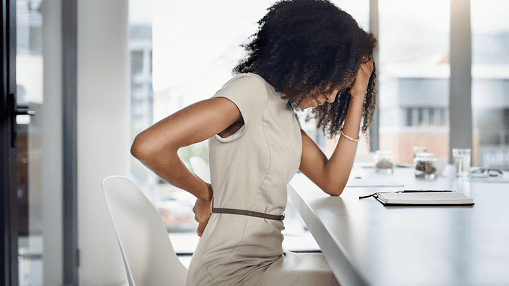 Woman experiencing discomfort while seated at a desk, illustrating challenges faced by individuals managing Irritable Bowel Syndrome (IBS).
