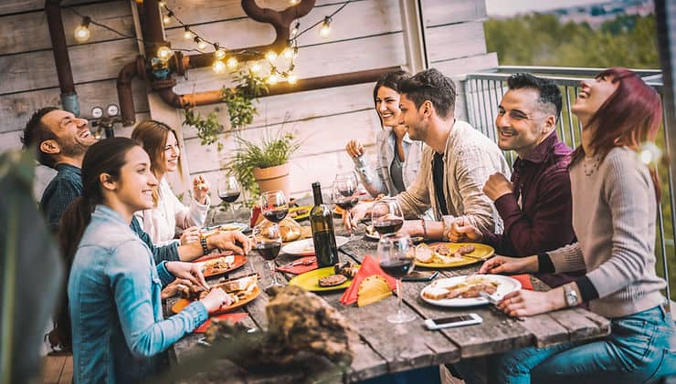 Group of friends enjoying a meal outdoors at a wooden table, featuring plates of food, glasses of wine, and a relaxed atmosphere, illustrating social dining experiences relevant to managing IBS.
