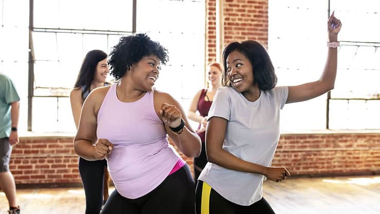 Two women dancing joyfully in a fitness class, promoting exercise for IBS relief and overall gut health.